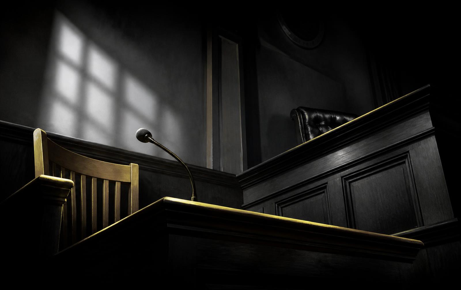 Empty courtroom witness stand lit by a single shaft of light